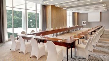 A conference room with a long table, white chairs, and large windows.