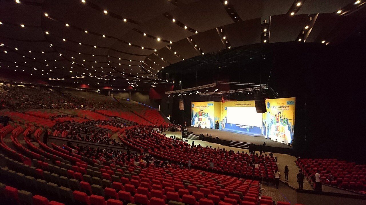 Un amplio auditorio interior con asientos escalonados y un escenario al frente.