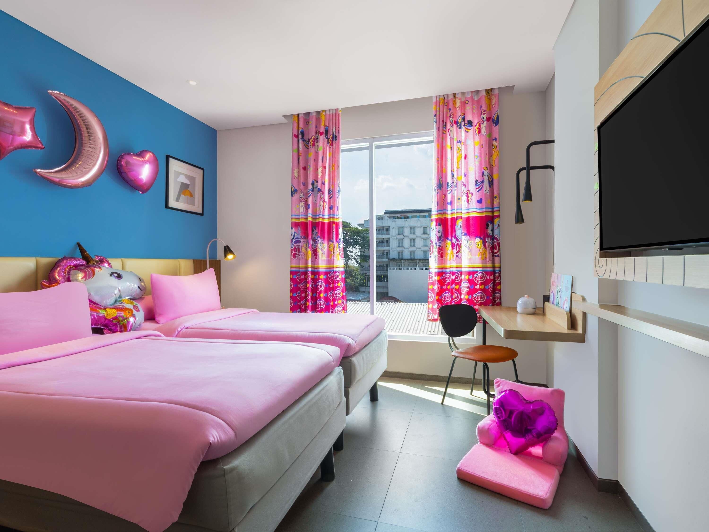 A bedroom with two beds, a desk, a TV, and colorful curtains.