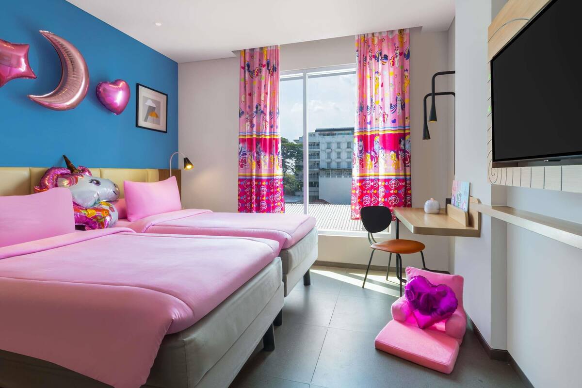 A bedroom with two beds, a desk, a TV, and colorful curtains.