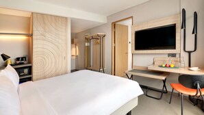 A hotel room with a bed, a desk with a chair, a TV, and a wardrobe. - ibis Styles Bogor Pajajaran (Bogor)