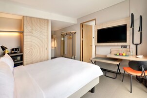 Una habitación de hotel con una cama, un escritorio con una silla, un televisor y un armario.