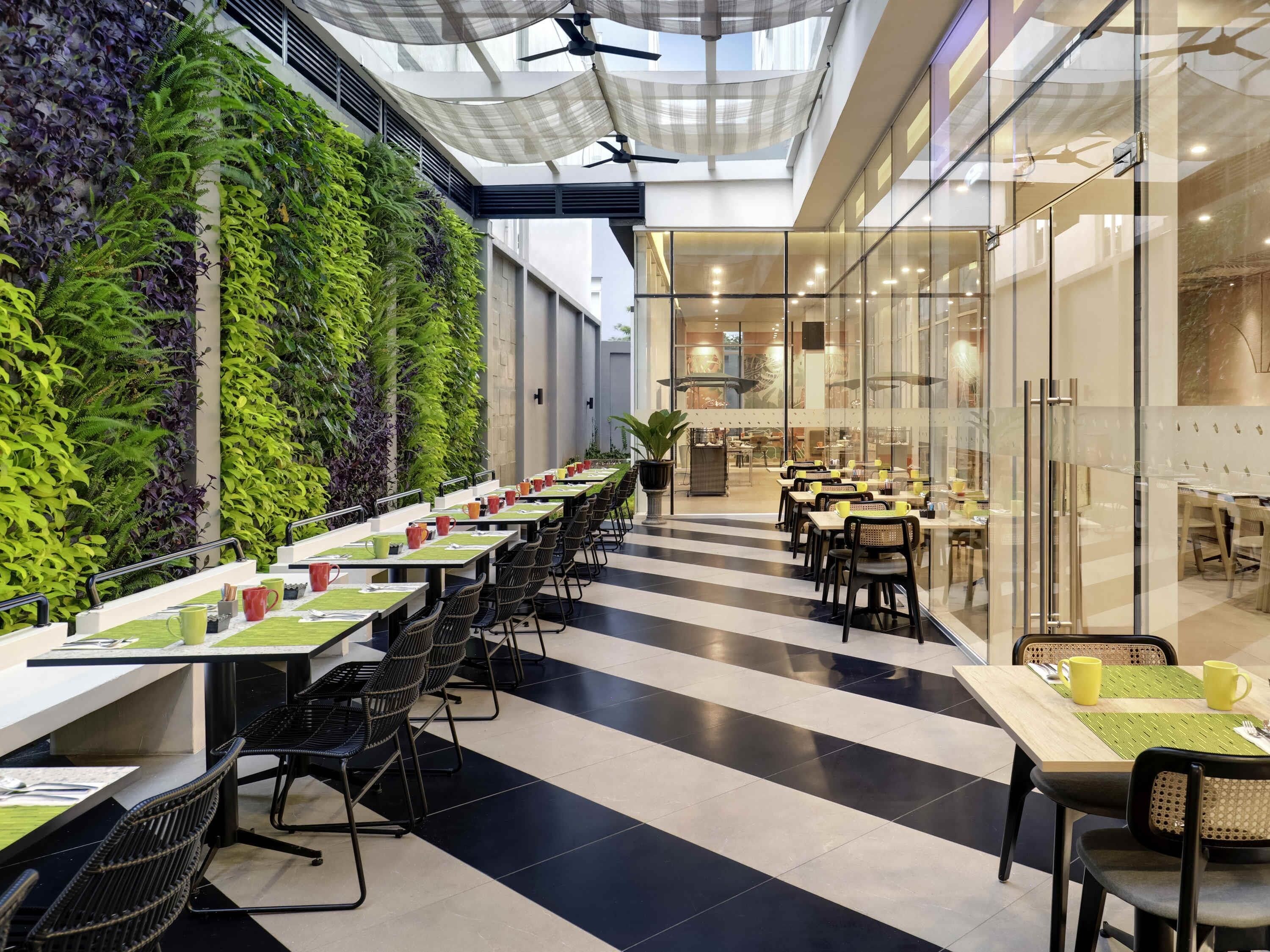 A modern dining area with long tables, chairs, and a green vertical garden wall.