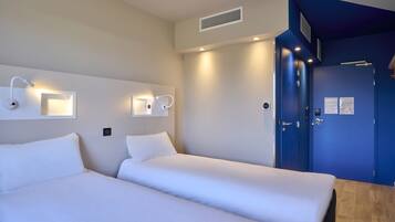 Une chambre d’hôtel avec deux lits, une porte bleue et des luminaires fixés au mur.