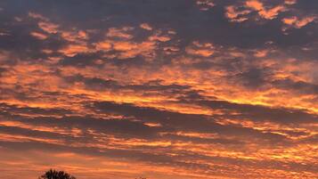 Un coucher de soleil avec des nuages orangés au-dessus d’un paysage vallonné.