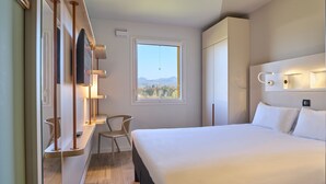 Une chambre d’hôtel moderne dotée d’un grand lit, d’un téléviseur fixé au mur, d’une fenêtre donnant sur les montagnes et d’un bureau avec une chaise.