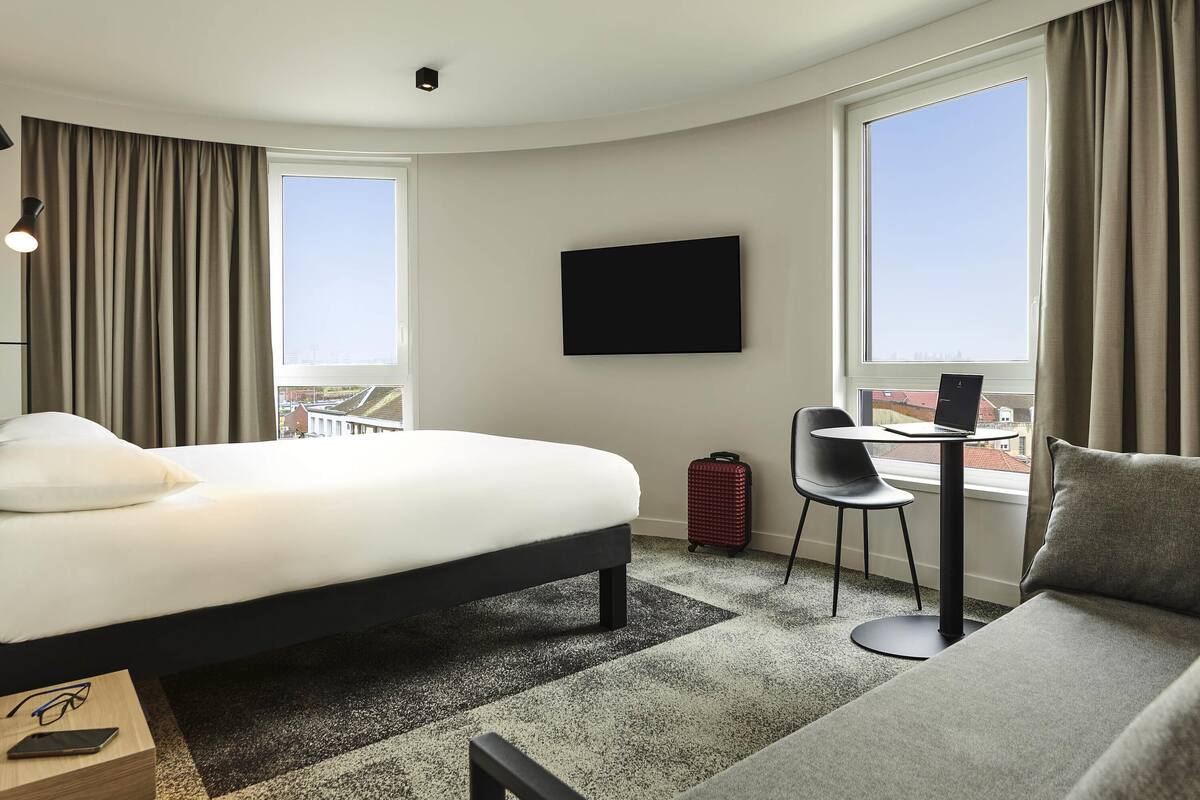 Une chambre d’hôtel avec un lit, un bureau avec un ordinateur portable, une chaise et un canapé.