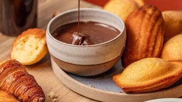 Un tazón de salsa de chocolate, pasteles y una taza de café sobre una superficie de madera.