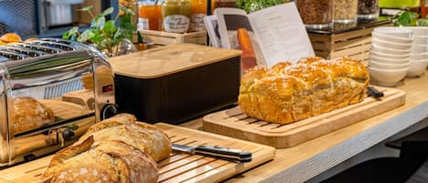 Un bufé de desayuno con panes variados, un tostador y un dispensador de zumo.