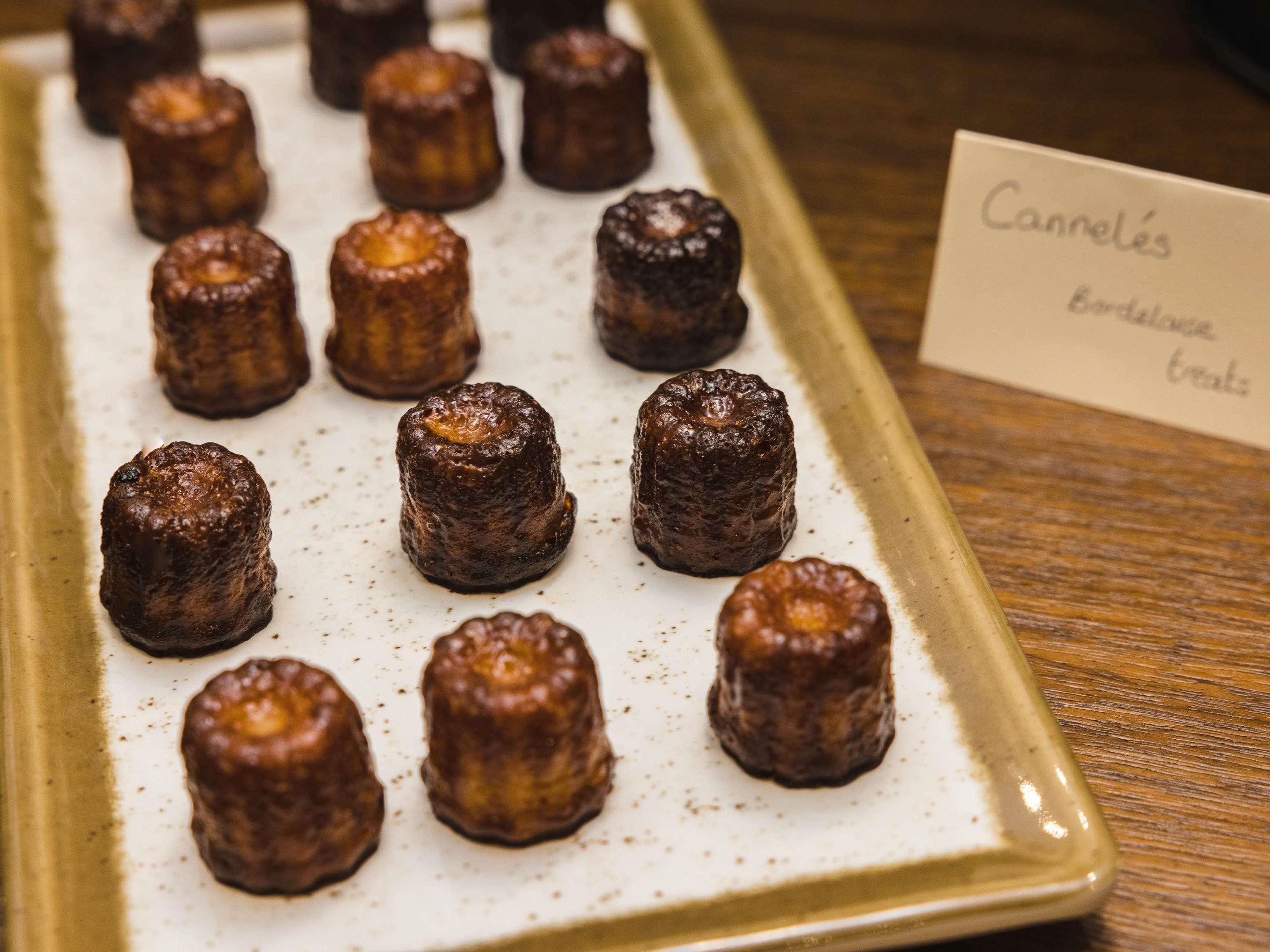Una bandeja de canelés sobre un plato de cerámica con un cartel que indica que son un tipo de dulce.