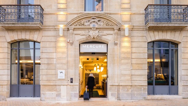 De ingang van het Mercure Hotel, met een statig gevelontwerp, grote ramen en een gastvrij interieur.