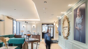 A modern hotel lobby with a green sofa, a round table with a vase, and a large mirror on the wall. - Mercure Bordeaux Centre Gare Atlantic (Bordeaux)