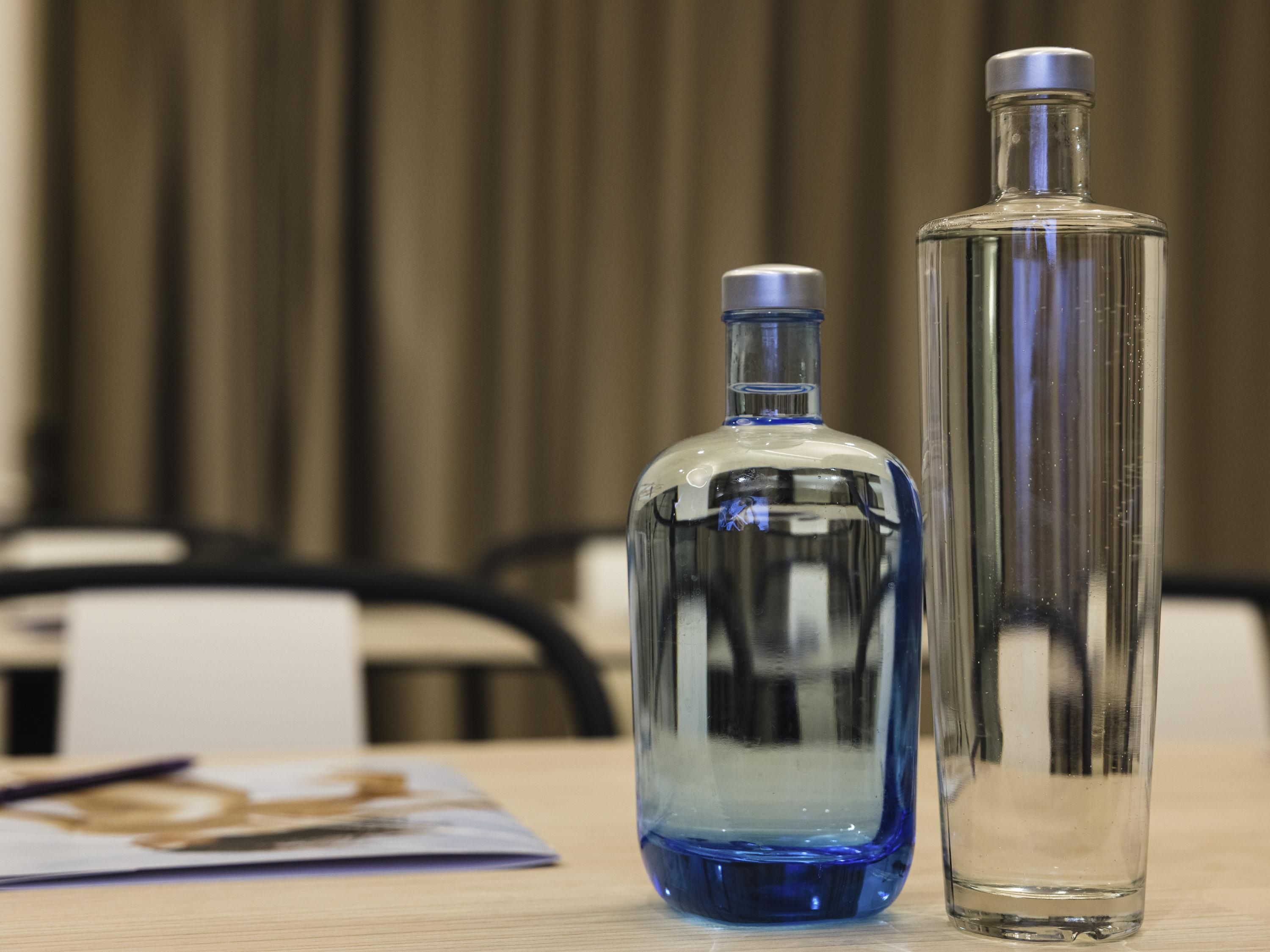 Dos botellas de vidrio transparente sobre una mesa de madera, con un fondo desenfocado.
