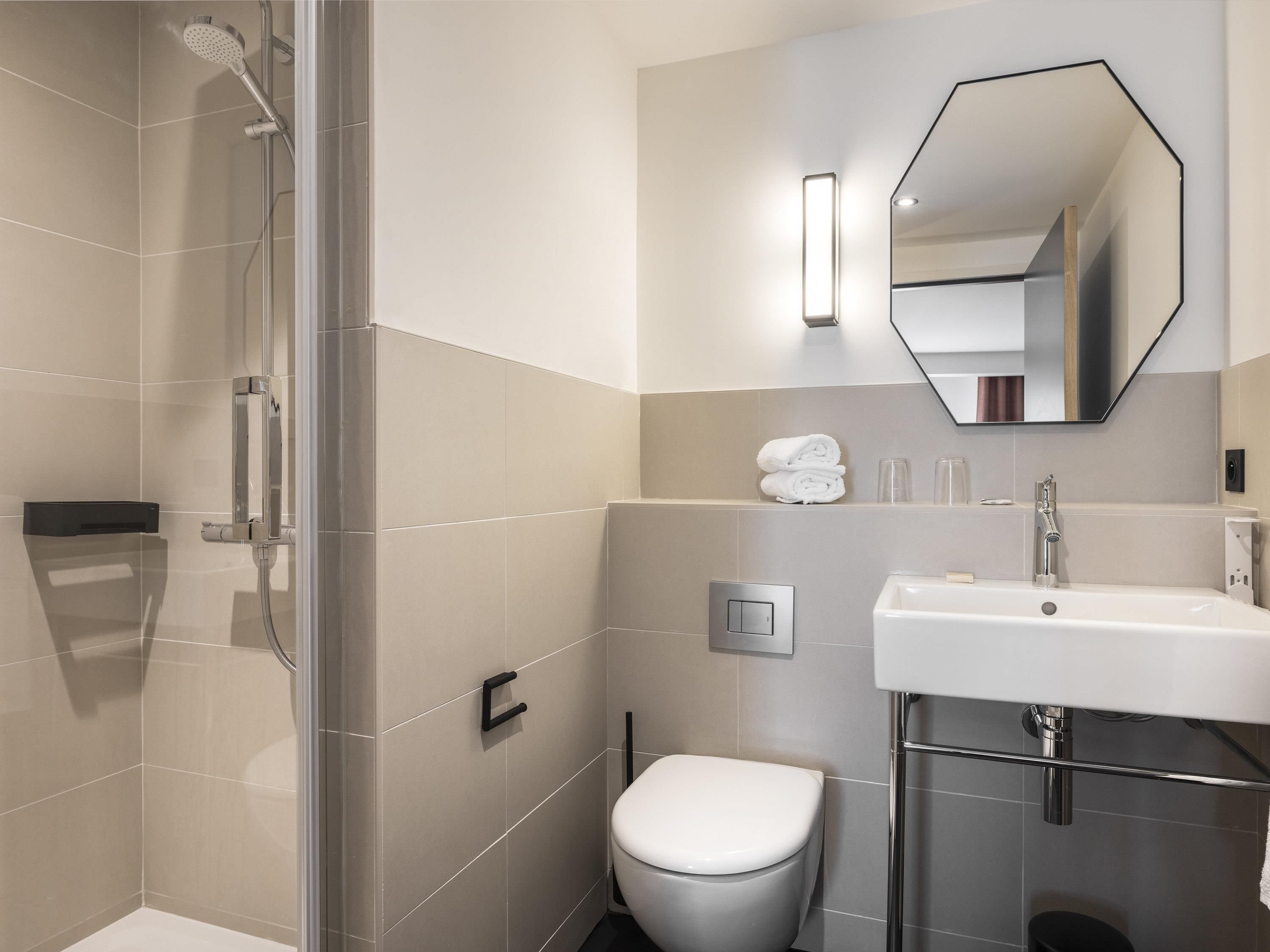 Une salle de bain moderne dotée d’une douche, de toilettes et d’un lavabo, avec des lignes épurées et des couleurs neutres.