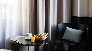 Una habitación de hotel con una mesa redonda pequeña donde se sirve el desayuno, con croissants, una taza de café y un vaso de zumo de naranja.