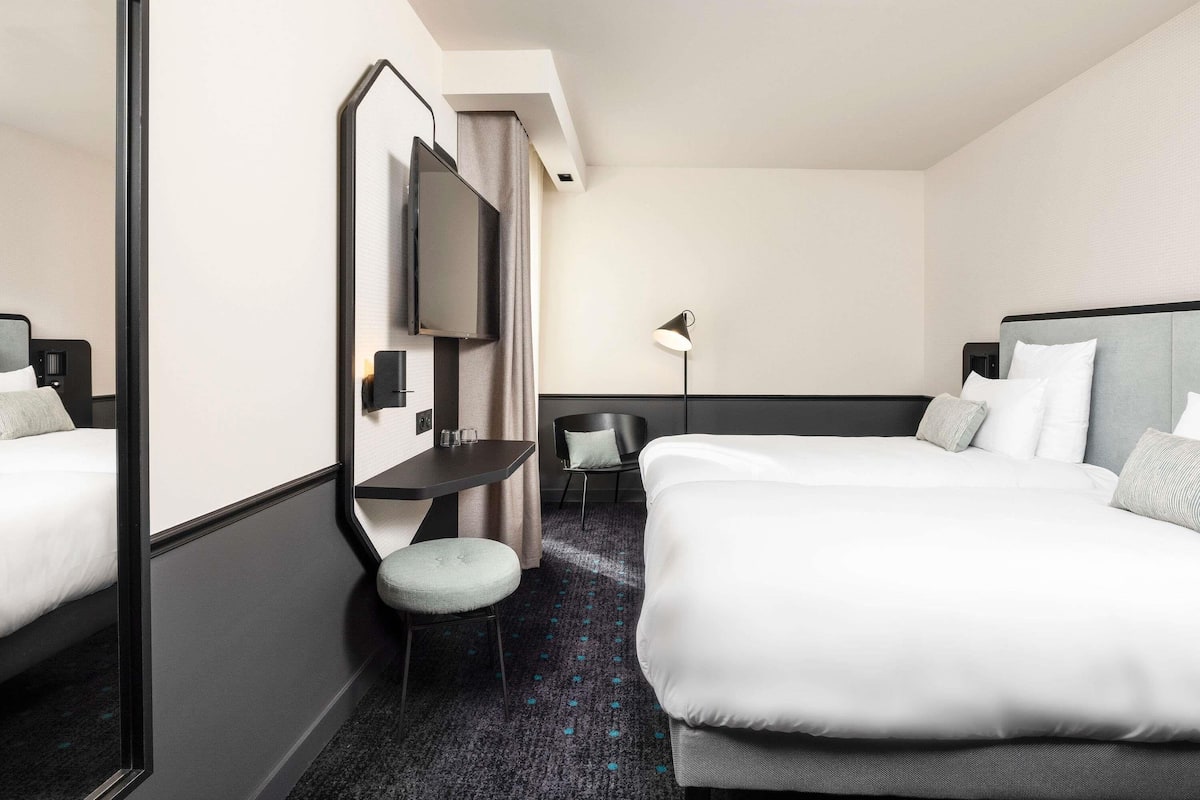 A hotel room with a bed, a desk, a chair, a TV, and a lamp.