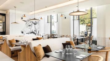 Interior modern d'un restaurant amb sostres alts, il·luminació penjant i un mural gran a la paret.