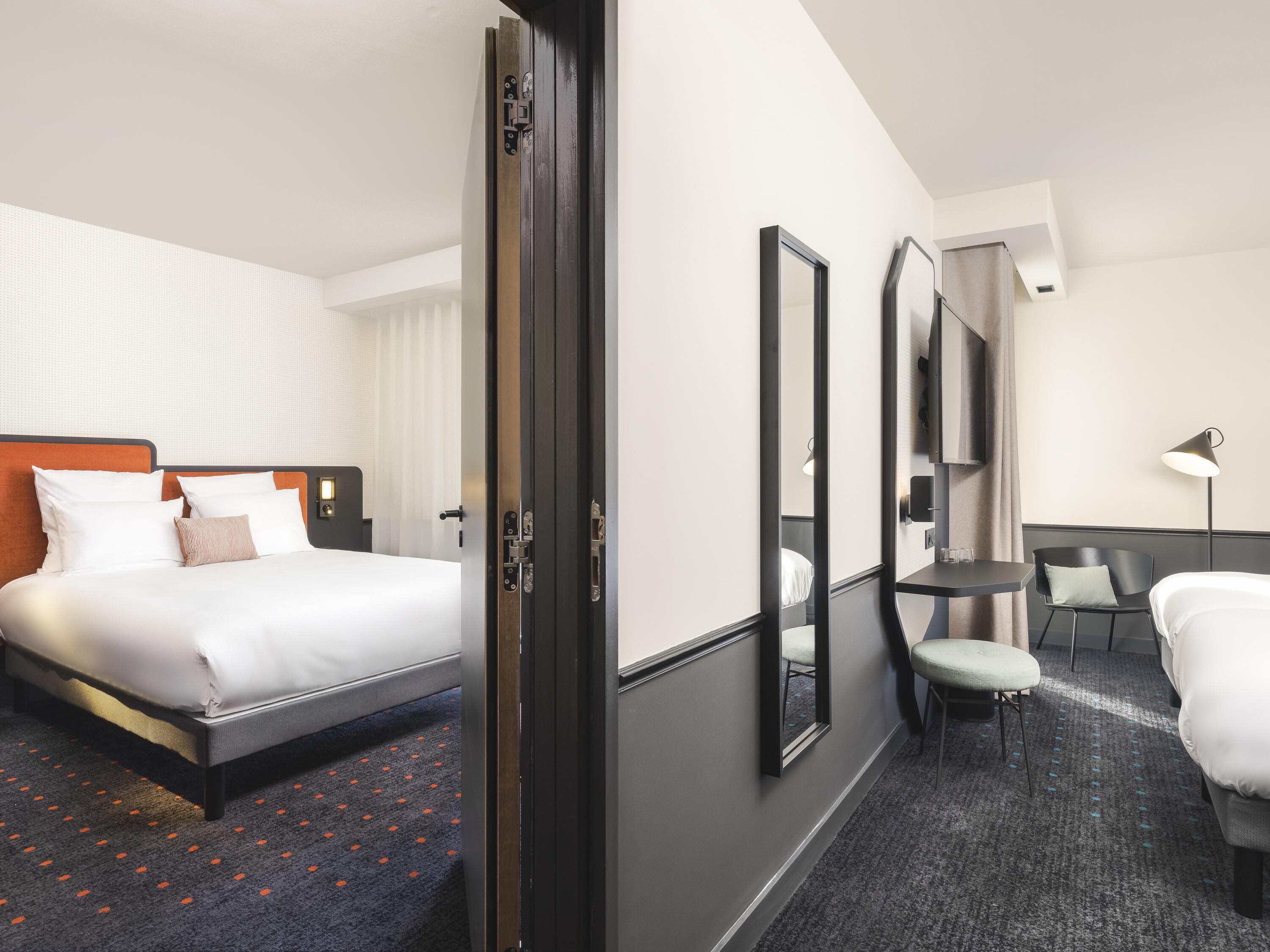A hotel room with a bed, a desk, a chair, and a mirror.