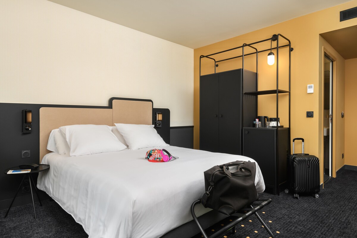 A hotel room with a bed, a desk, a wardrobe, and a suitcase.