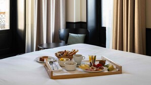 Een hotelkamer met een keurig opgemaakt ontbijttafel op het bed, met croissants, fruit en een glas sinaasappelsap.