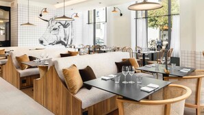 Een modern restaurantinterieur met hoge plafonds, hanglampen en een groot muurschildering.