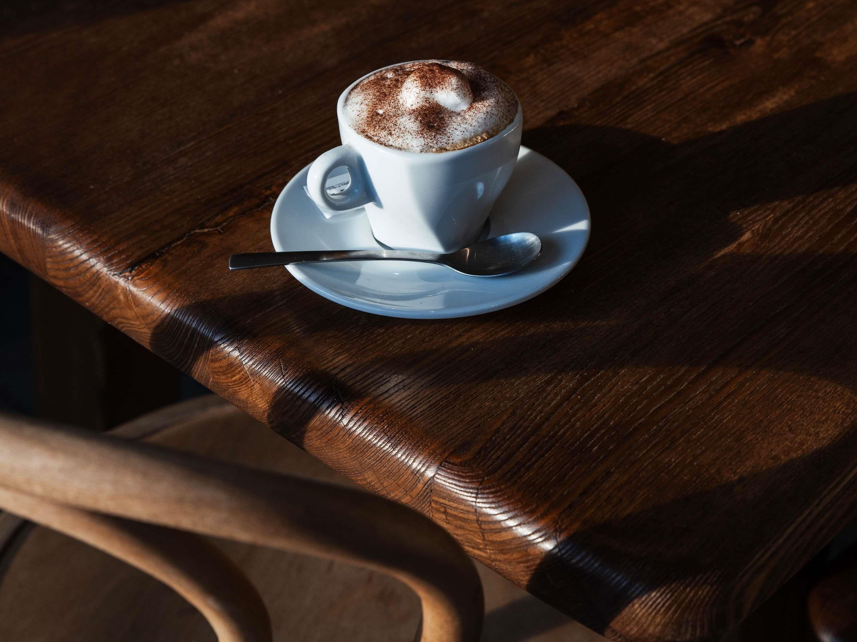 A cup of coffee on a saucer with a spoon, placed on a wooden table.