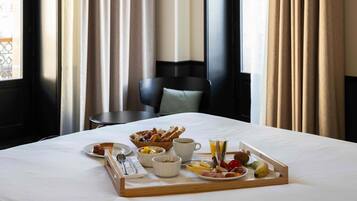 A hotel room with a neatly made breakfast tray on the bed, including croissants, fruits, and a glass of orange juice.