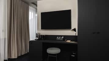 A modern hotel room with a dark desk, a flat-screen TV, a small stool, and a wardrobe.