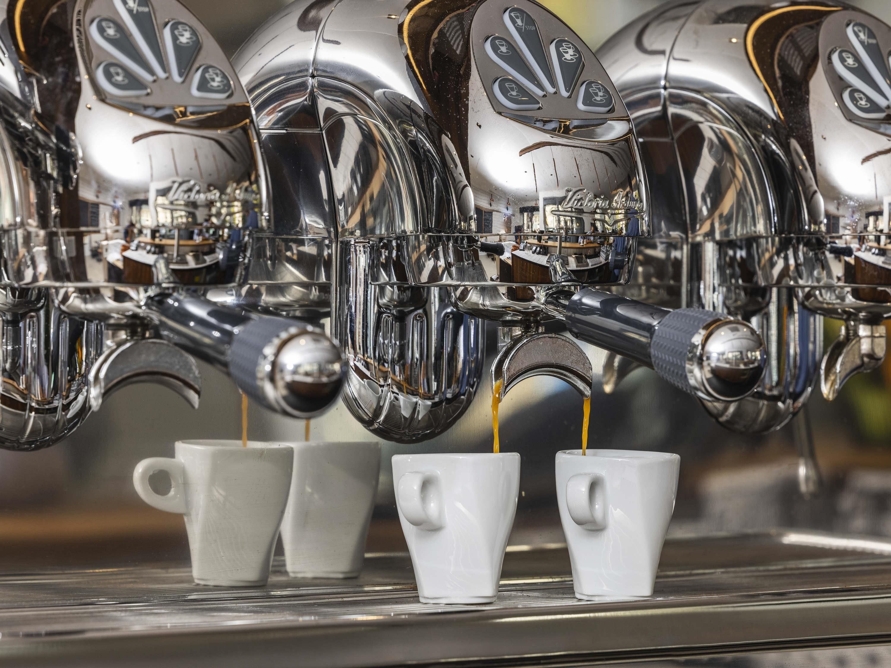 Una cafetera con varios surtidores vertiendo café en tazas blancas.