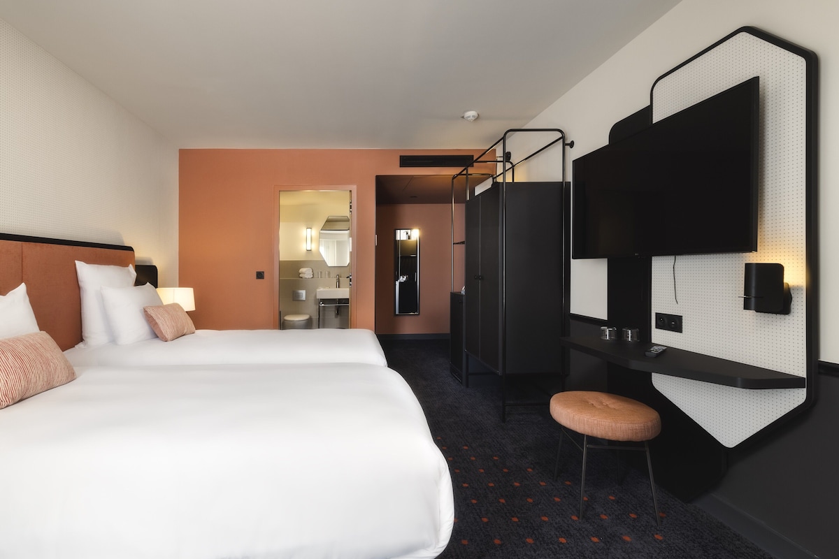 A hotel room with two beds, a desk, a chair, a mirror, and a TV mounted on the wall.