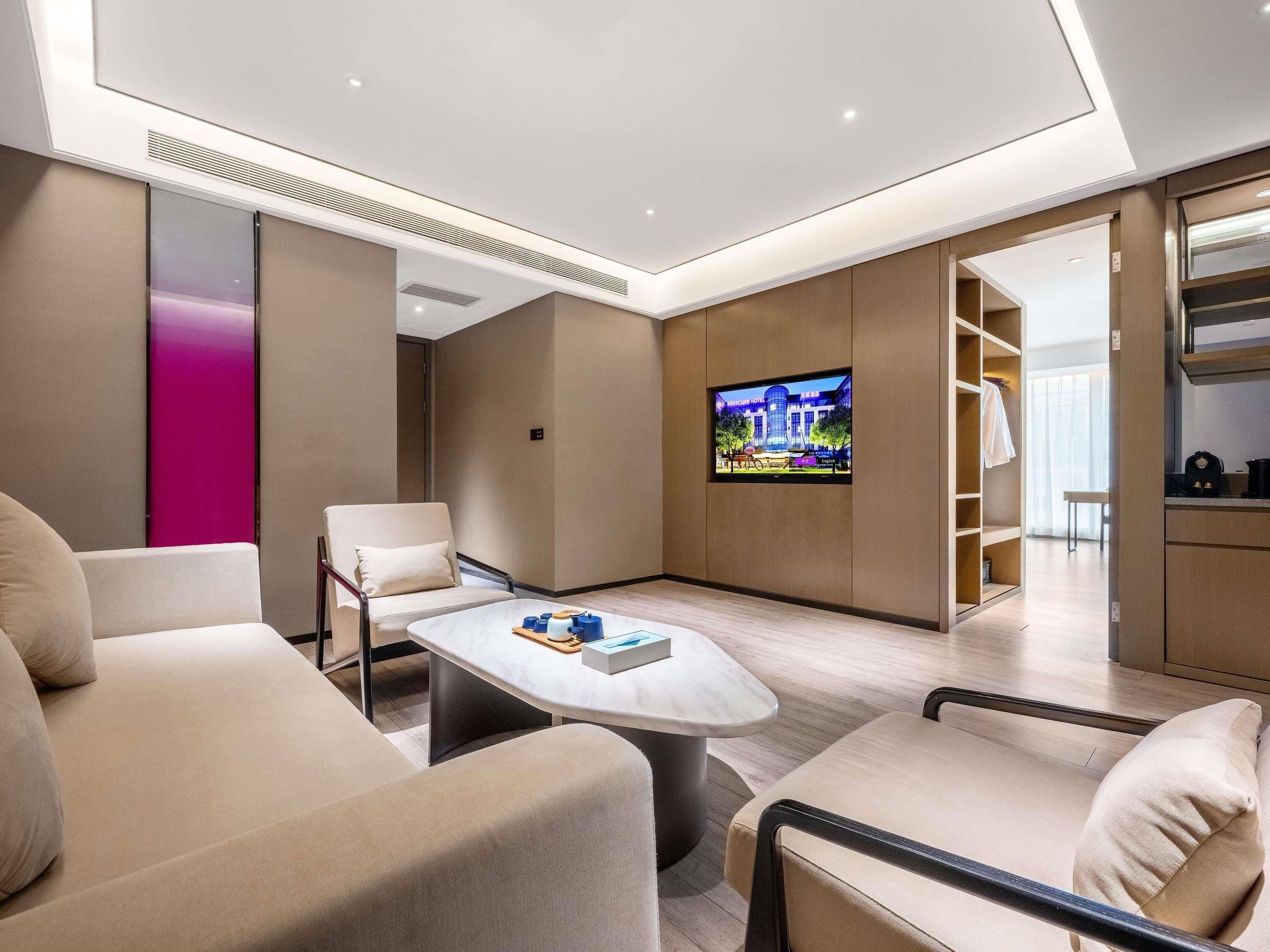Habitació d'hotel moderna amb un televisor de pantalla plana penjat a la paret, un sofà, una taula de cafè i una petita cuina.