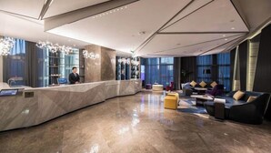 A modern lobby with a curved reception desk, seating area with sofas and ottomans, and large windows with curtains.