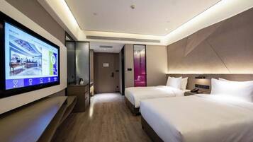 Habitación de hotel con una televisión grande en la pared, dos camas, una mesita de noche y una puerta que da a otra habitación.