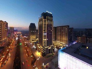 Un edificio alto con varios pisos, rodeado de otros edificios y calles concurridas.