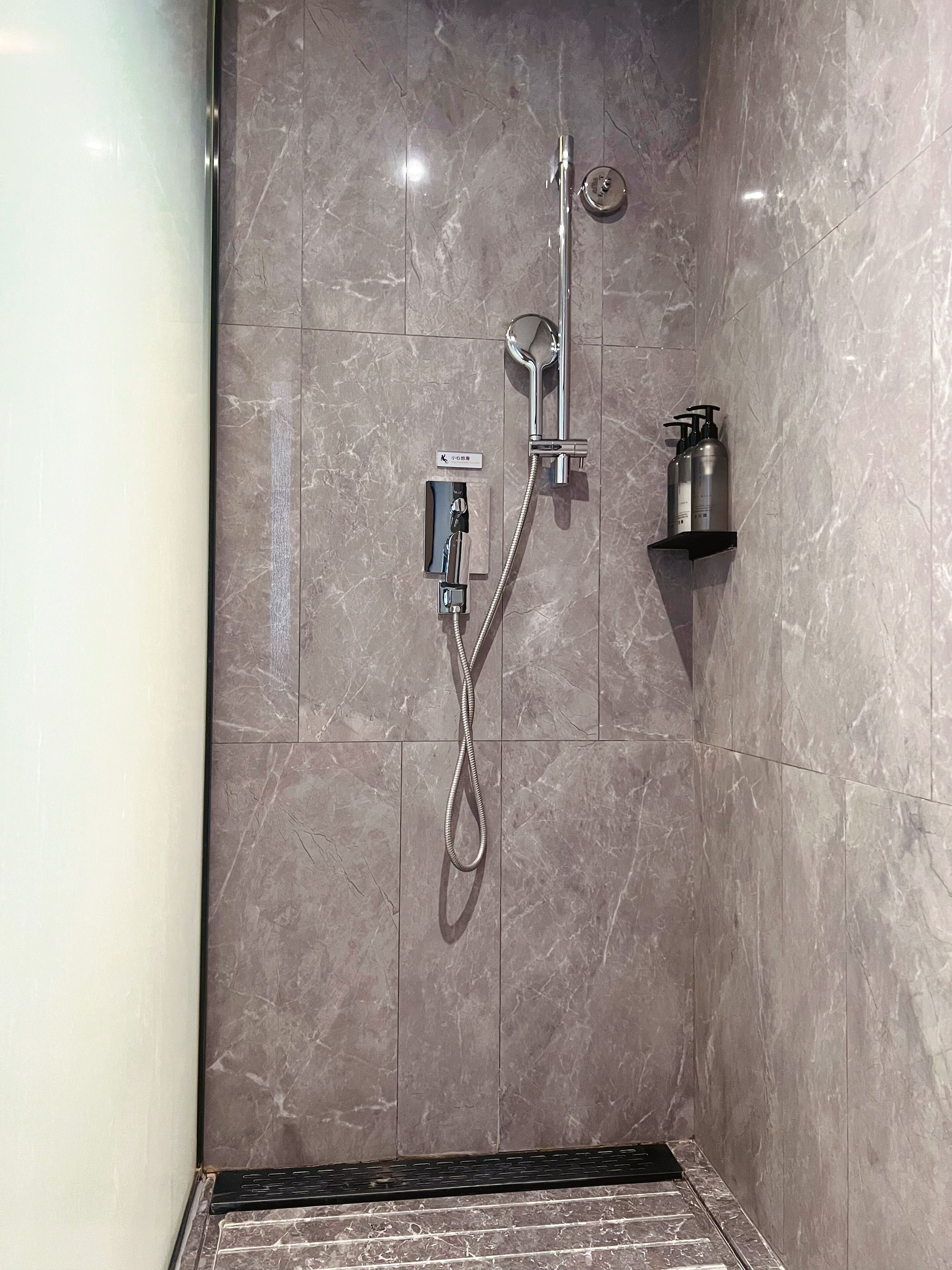 Ducha con cabezal de ducha de mano, grifo empotrado y dispensador de jabón.