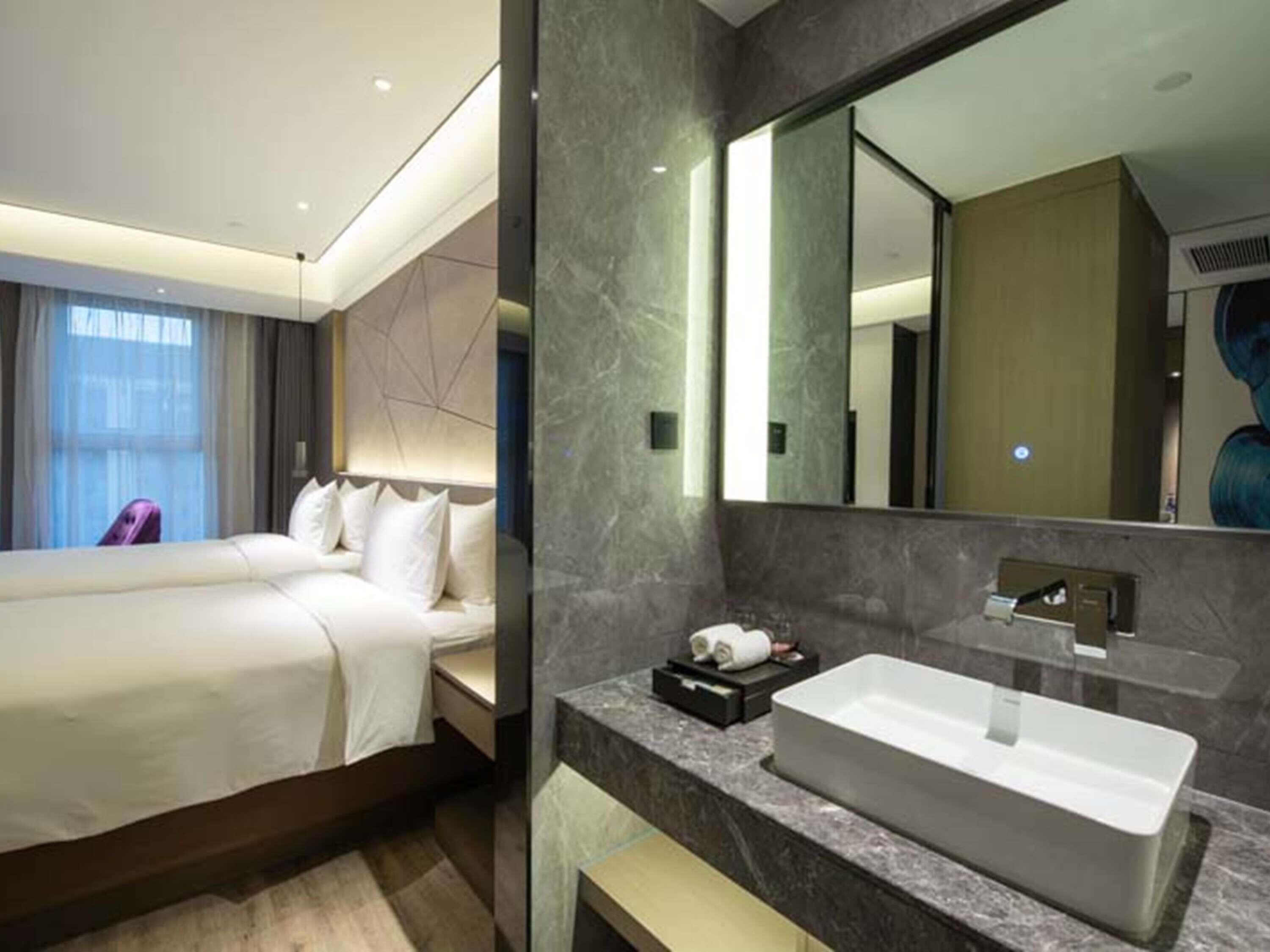 A hotel room with a bed, a large mirror, a marble countertop, and a sink.