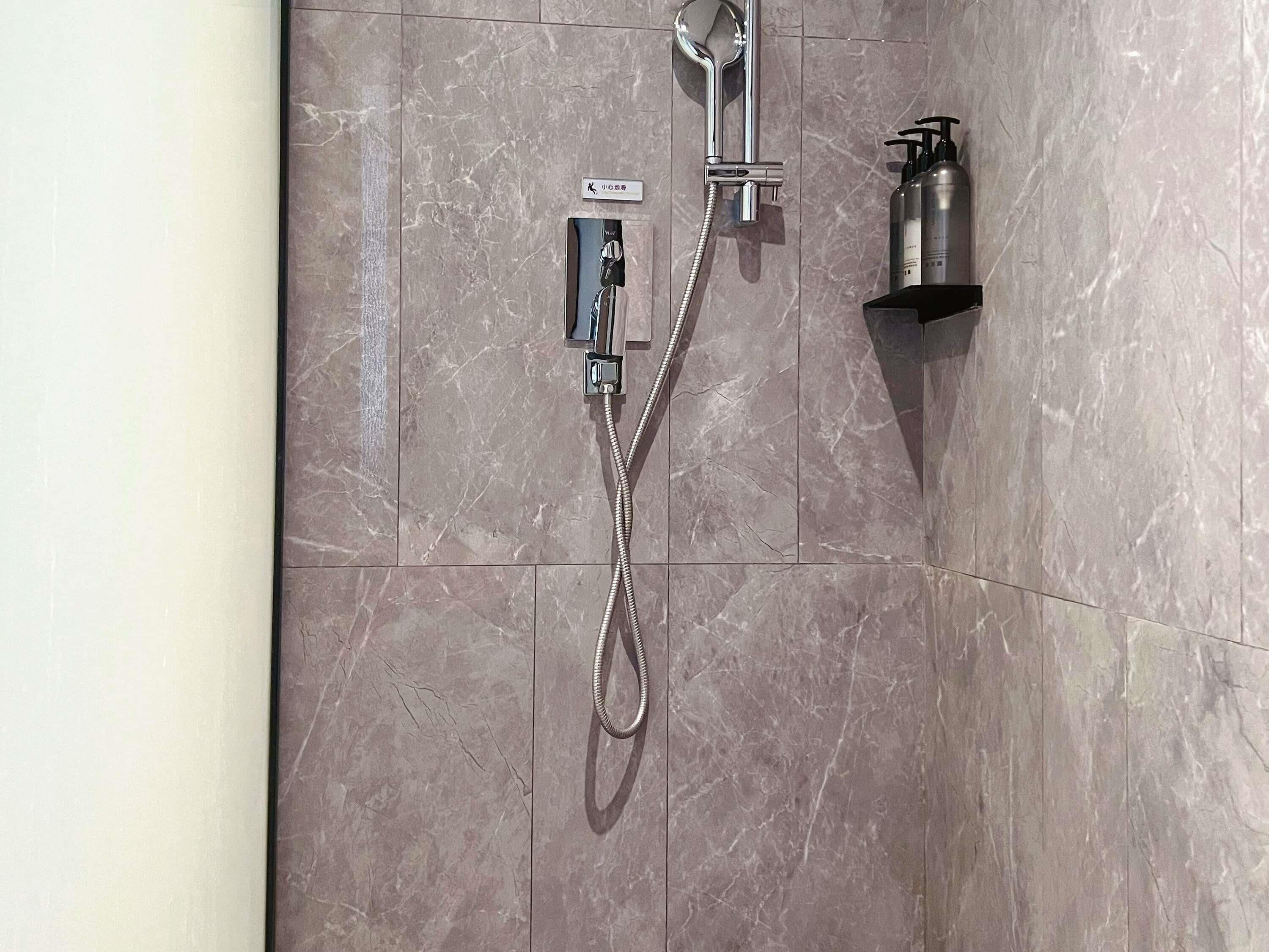 A shower with a handheld showerhead and a wall-mounted control panel.