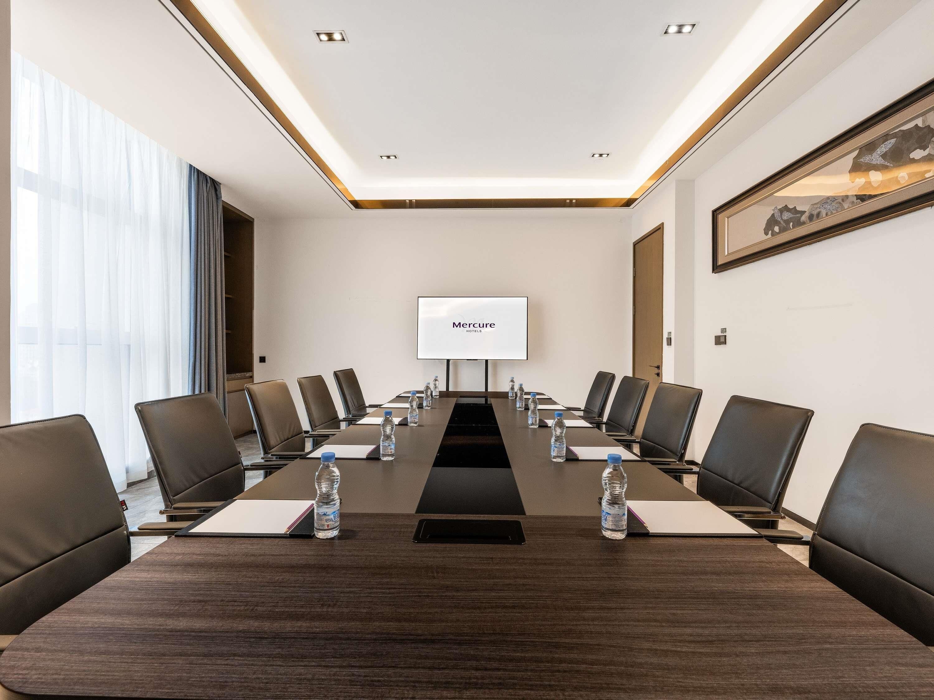 A conference room with a long table, chairs, a projector screen, and water bottles.