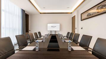 A conference room with a long table, chairs, a projector screen, and water bottles.