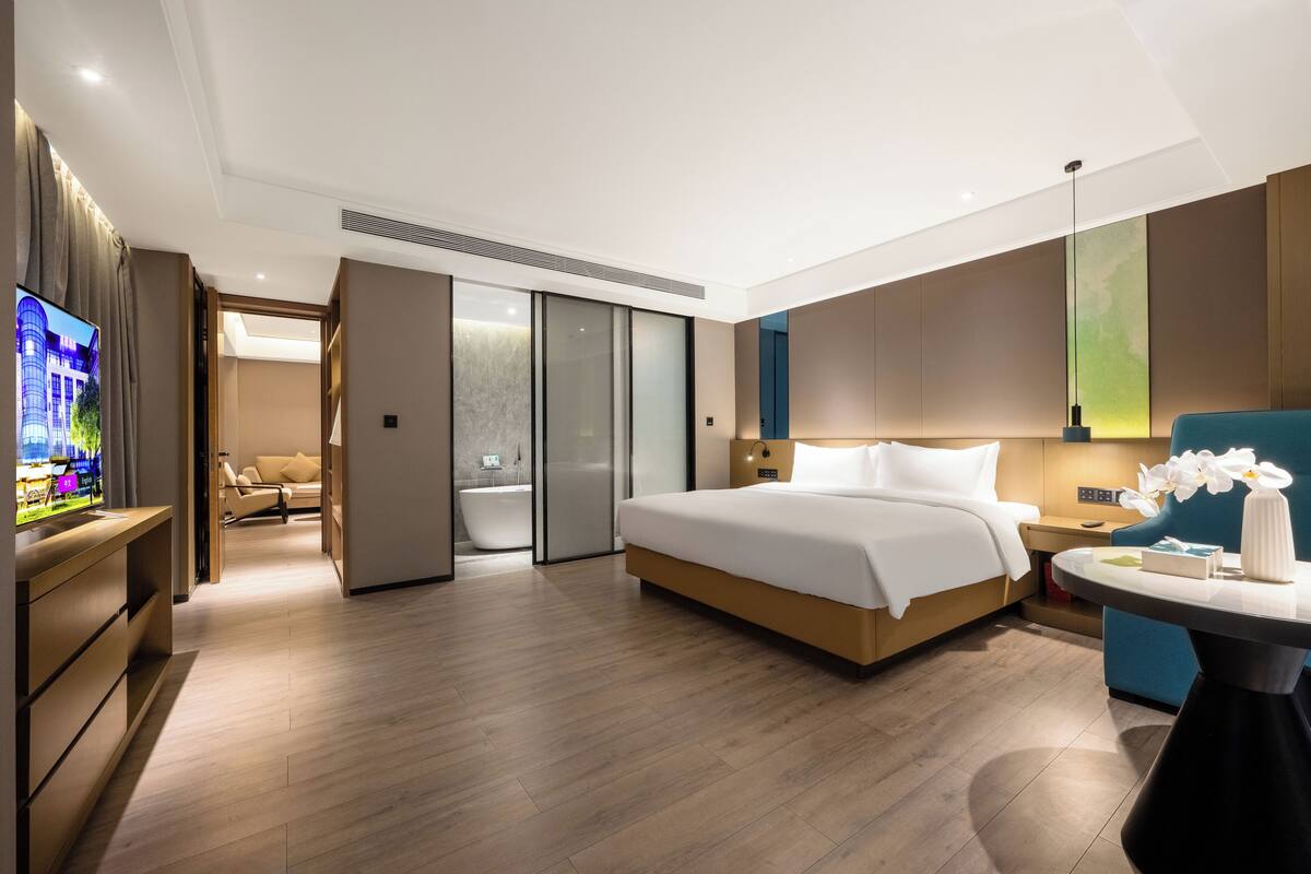 A modern hotel room with a large bed, a TV, a desk, and a bathroom with a bathtub.