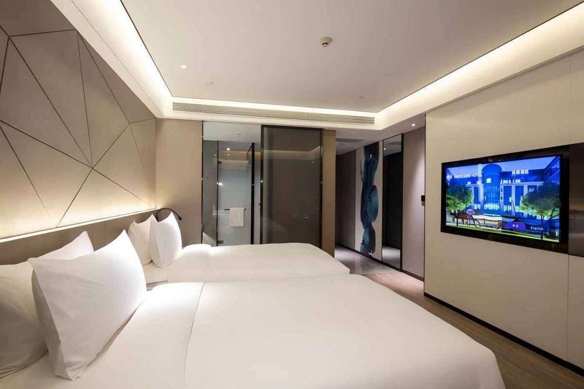 A modern hotel room with a large bed, a television mounted on the wall, and a glass shower enclosure.