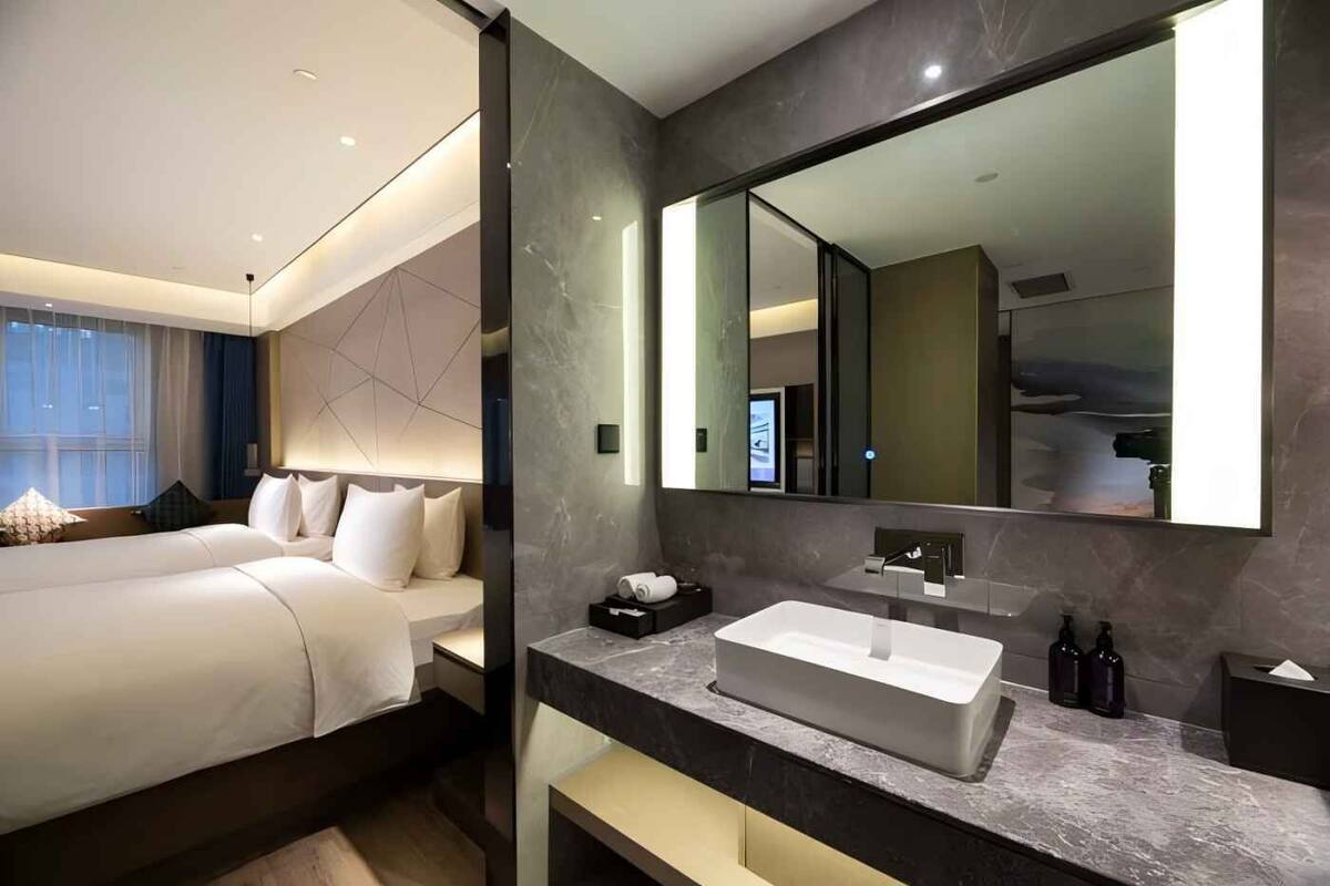 A modern hotel room with a large bed, a bathroom with a large mirror, and a marble countertop.