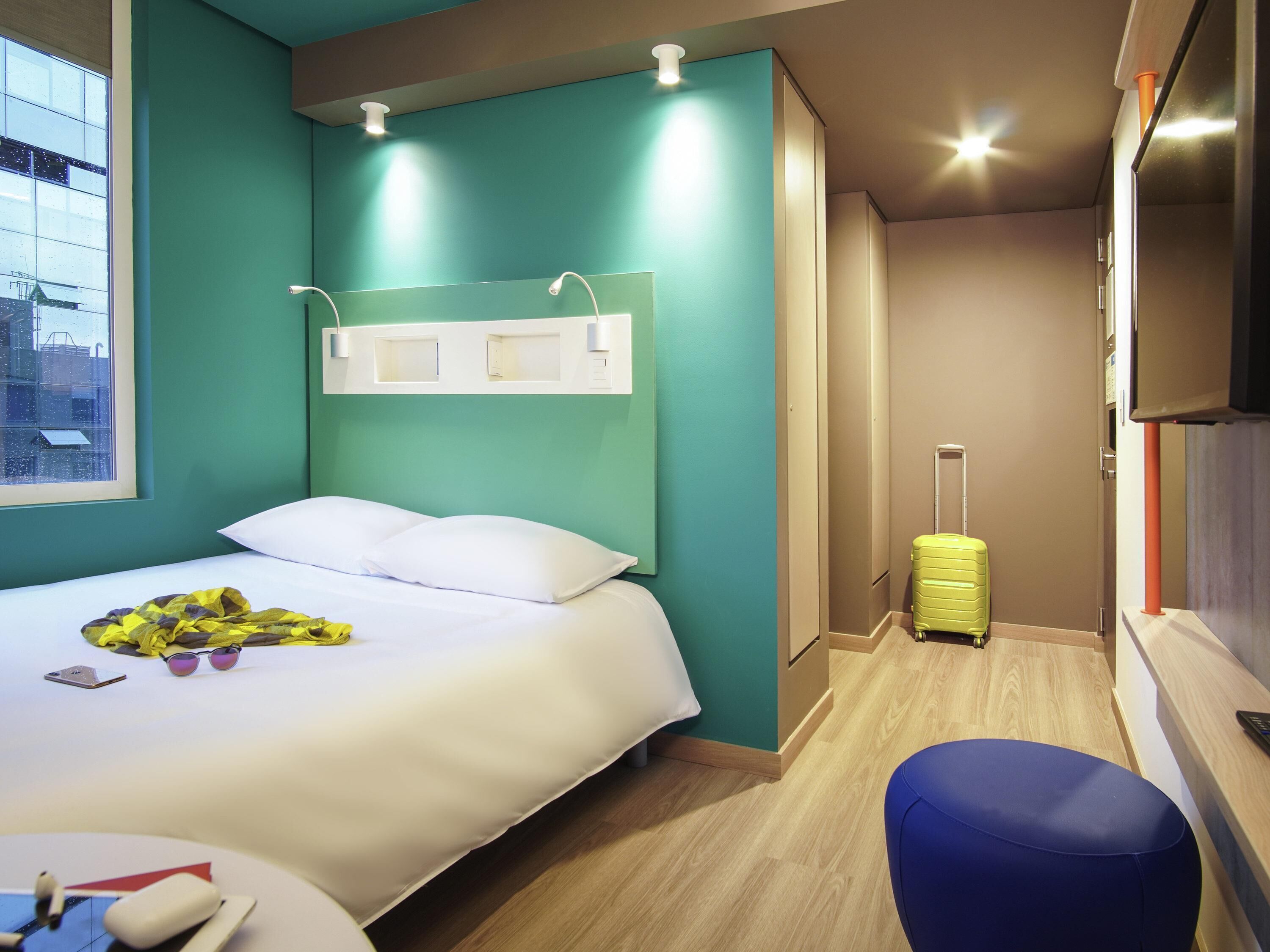 A hotel room with a bed, a suitcase, a desk with a chair, and a television.