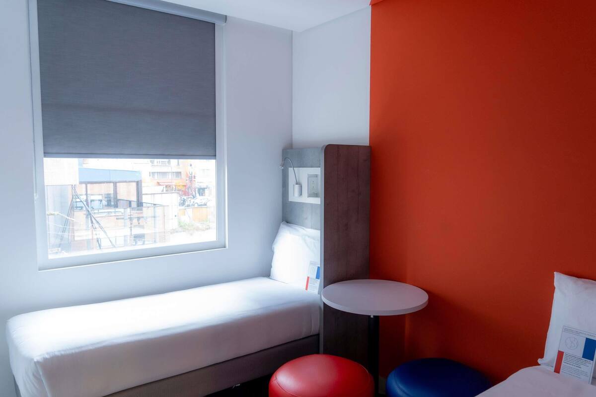 Ein Zimmer mit einem Bett, einem kleinen Tisch und zwei bunten Hocker.