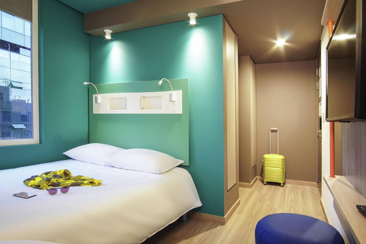Ein Hotelzimmer mit Bett, Koffer, Schreibtisch mit Stuhl und Fernseher.