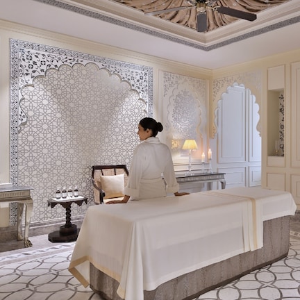 A luxurious hotel room with a large bed, ornate wall decorations, a vanity with a mirror, and a well-lit ambiance.