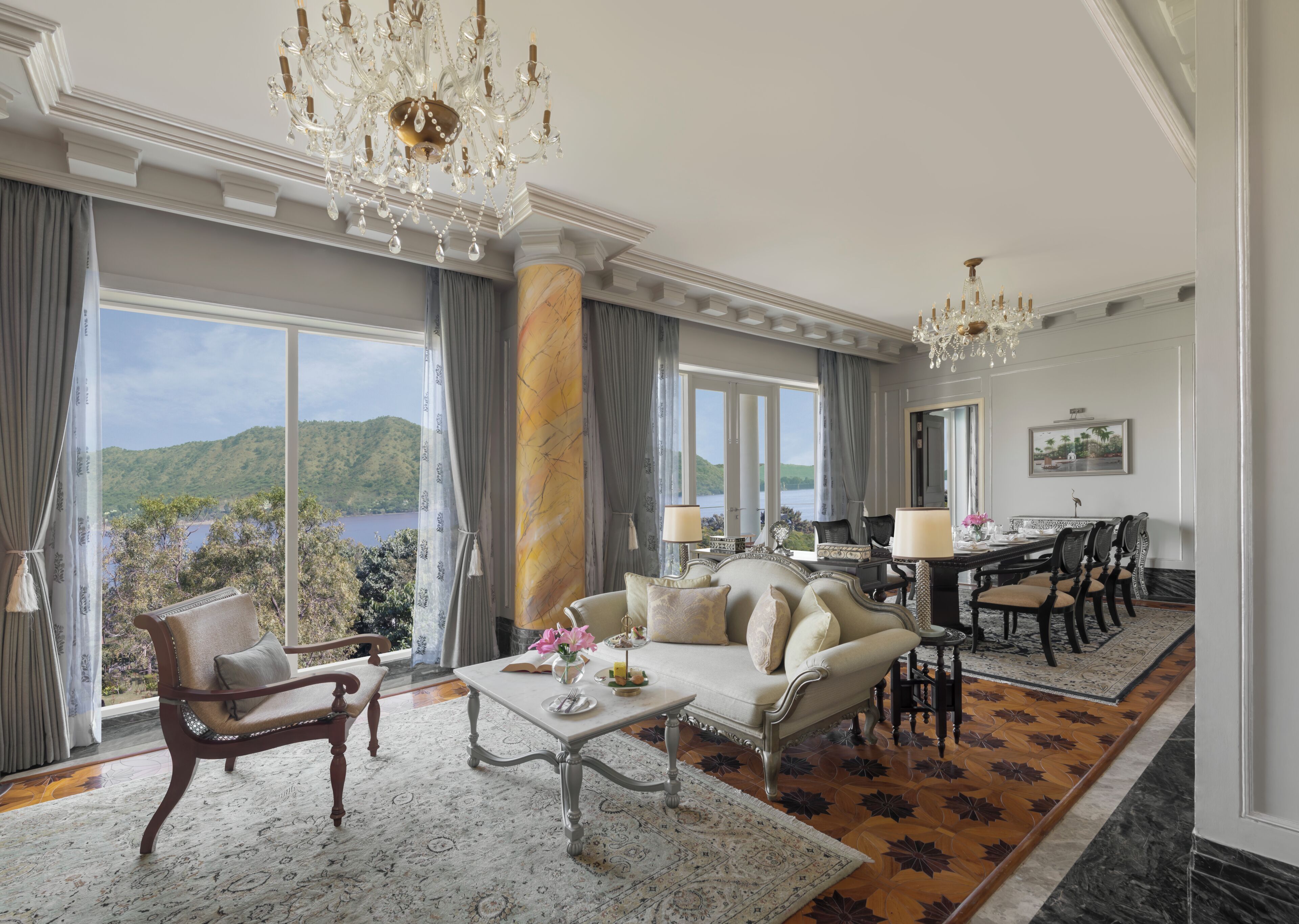 A spacious room with a large window, a dining area, and a chandelier.
