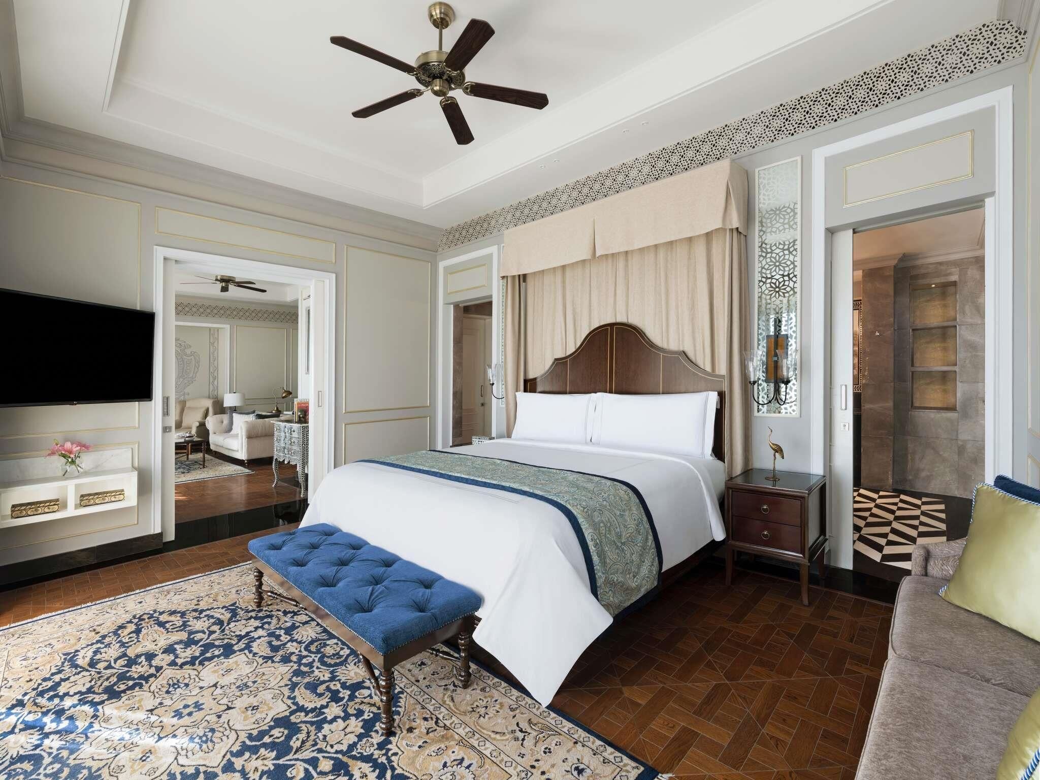 A hotel room with a large bed, a ceiling fan, a TV, a bedside table, and a patterned rug.