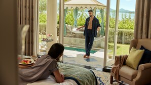 A hotel room with a bed, a sofa, a dining table with a plate of food, and a view of a pool and garden through a glass door. - Raffles Udaipur (Udaipur)