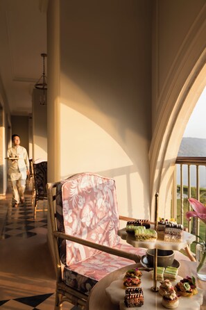 A room with a dining table set for a meal, a chair with a floral pattern, and a view of the outdoors.